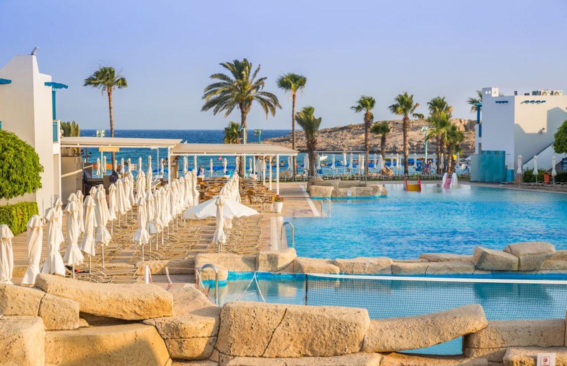 Poolbereich des Callisto Holiday Village mit Palmen und Meer im Hintergrund.