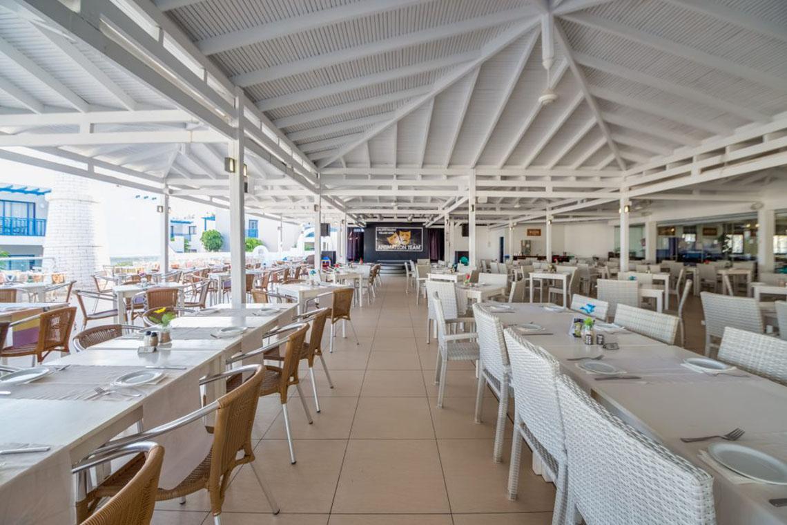 Innenansicht des Restaurants im Callisto Holiday Village mit leeren Tischen und Stühlen.