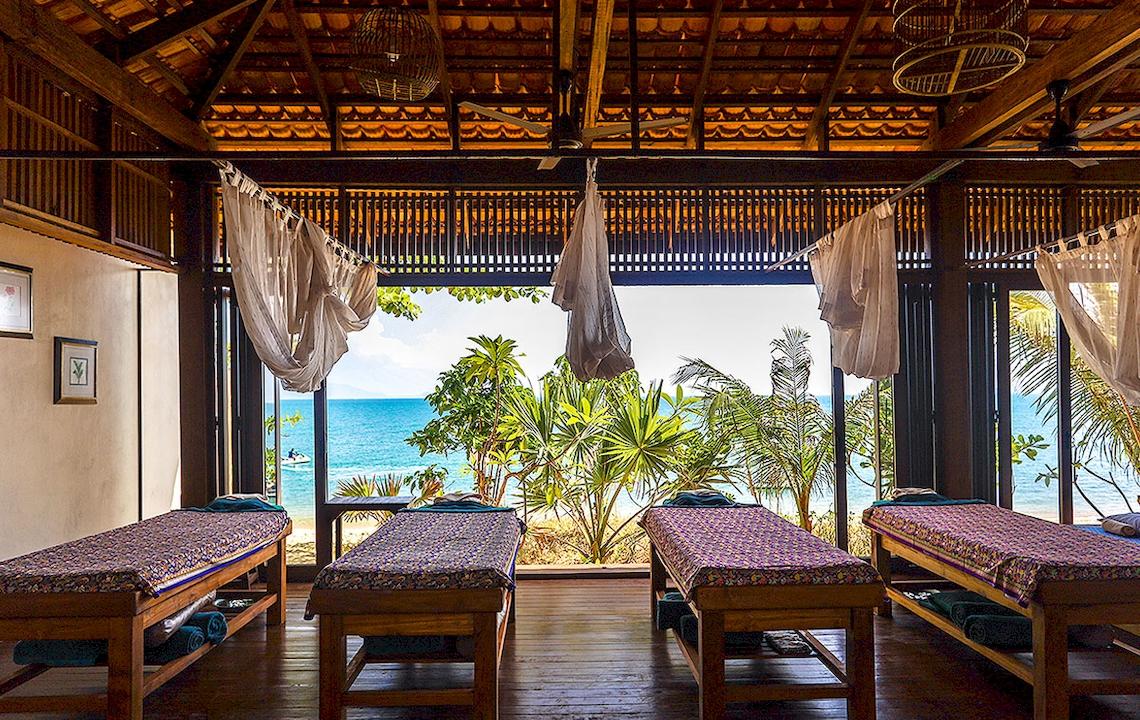 Massageraum im Saree Samui Resort mit Blick auf das Meer und Palmen.