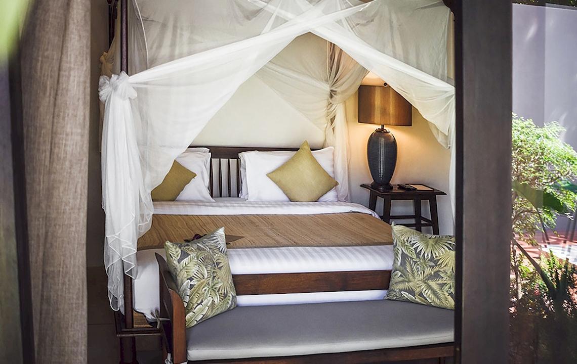 Bett mit Baldachin im Saree Samui Resort mit Kissen, Lampe und Tageslicht.
