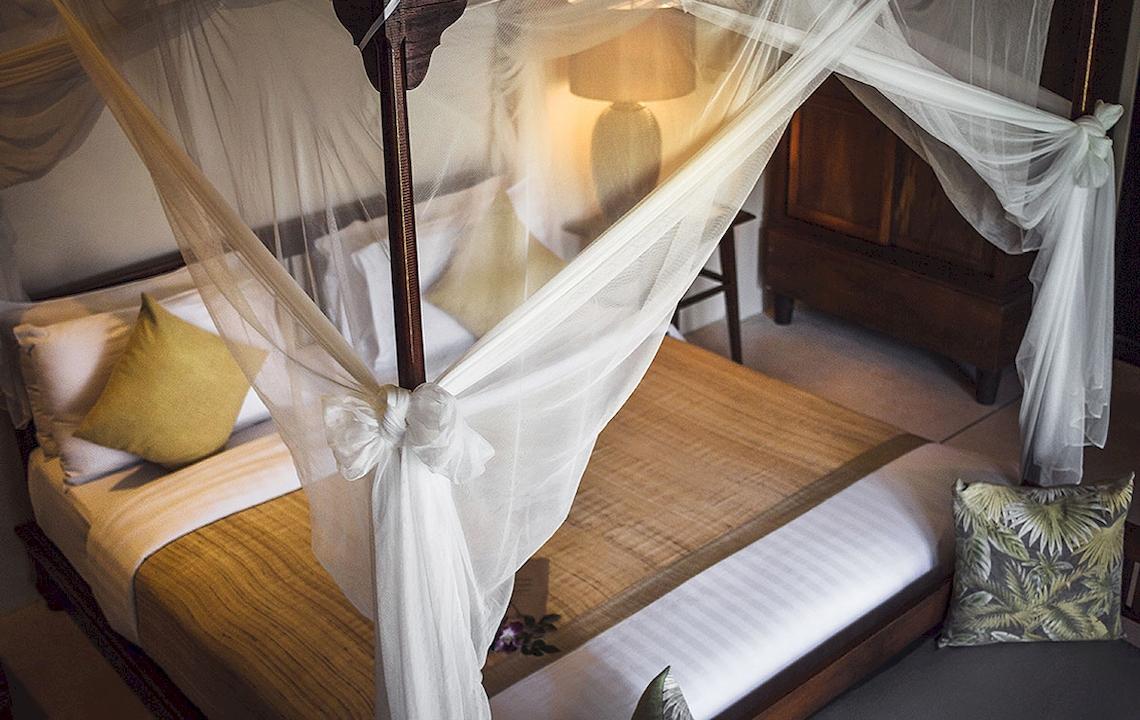 Ein Bett mit Baldachin im Saree Samui Resort, mit weißen Laken und gelben Kissen.