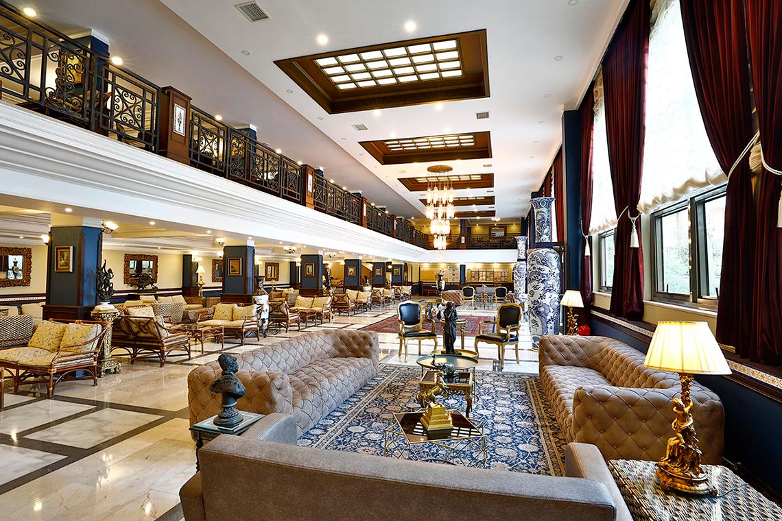 Club Yali Hotels & Resort Lobby mit gepolsterten Sofas, Kronleuchtern und großen Fenstern.
