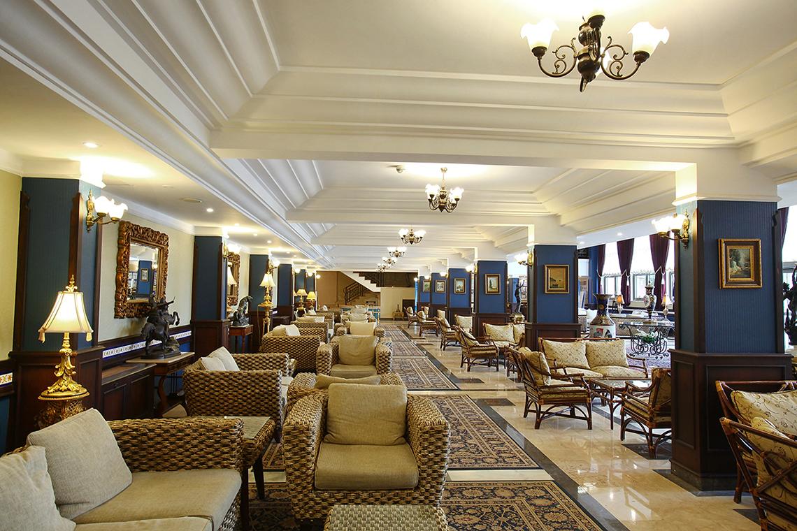 Innenansicht des Club Yali Hotels & Resort mit gepolsterten Stühlen und Sofas, Kronleuchtern und dekorativen Lampen.