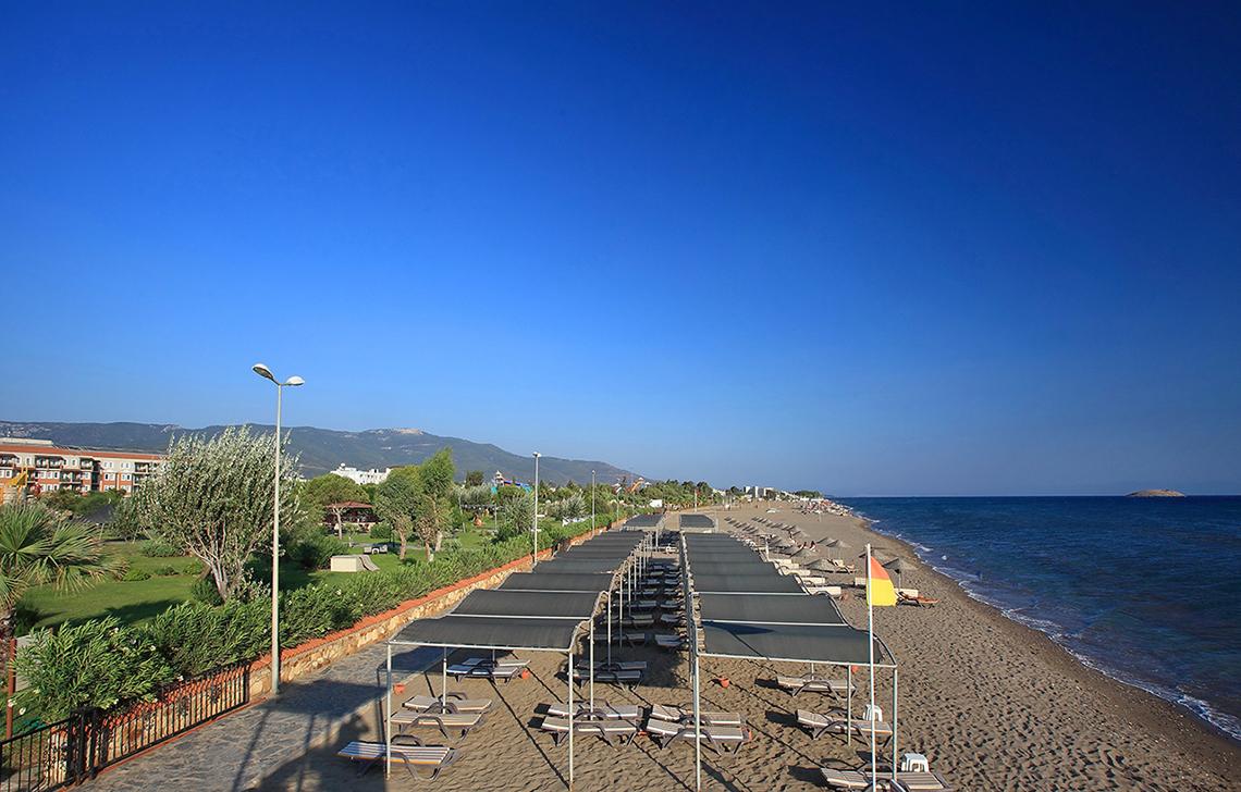 Strand des Club Yali Hotels & Resorts mit Sonnenliegen und Sonnenschirmen