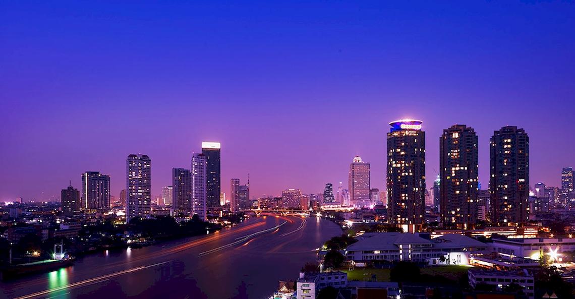Abendliche Stadtansicht von Bangkok mit dem Chatrium Hotel Riverside, das sich am Flussufer befindet.