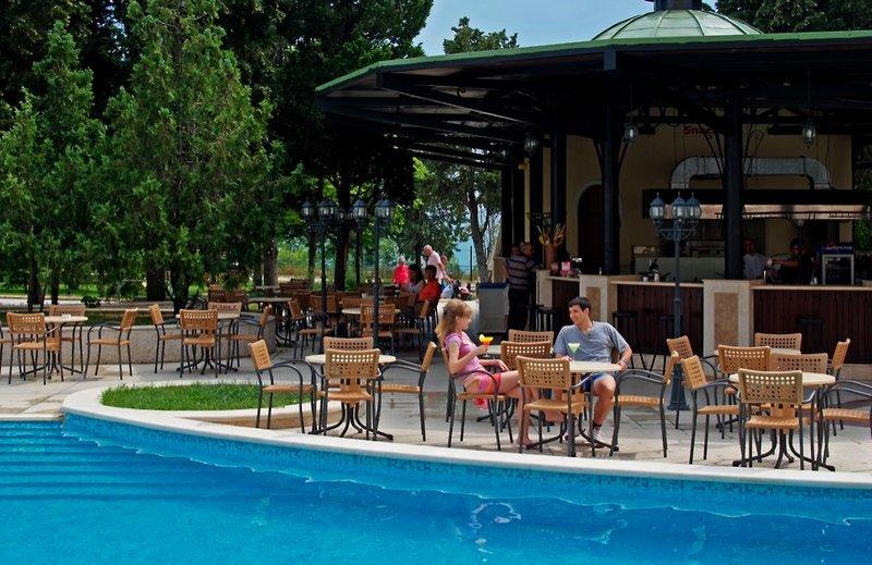 Gäste sitzen an einem Tisch vor einem Pool im Sol Nessebar Palace Hotel.