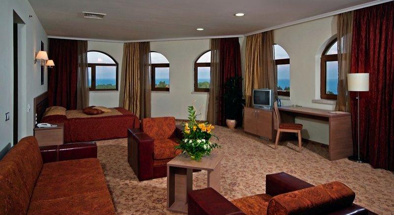 Hotelzimmer des Sol Nessebar Palace All Inclusive mit Bett, Sofa, Schreibtisch und Aussicht auf den Ozean.