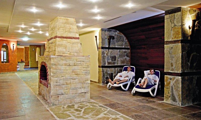 Relaxationsbereich im Sol Nessebar Palace All Inclusive Hotel mit zwei Personen auf Liegen neben einem Steinkamin