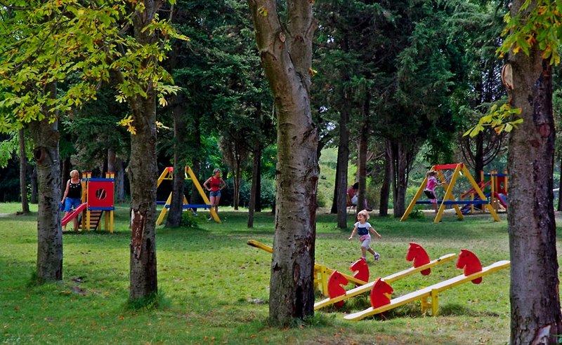 Kinderspielplatz im Freien im Sol Nessebar Palace Hotel mit Bäumen und Spielgeräten.
