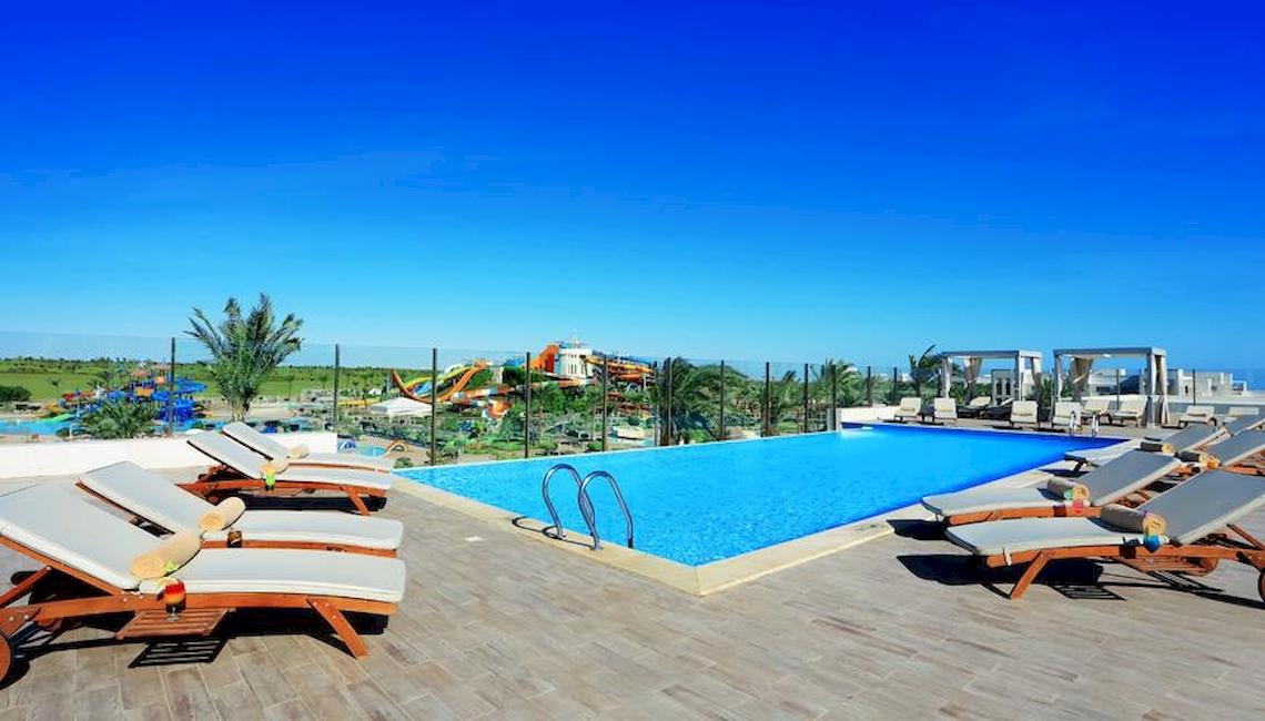 Ein Swimmingpool im Jaz Aquaviva Hotel mit Lounge-Liegen und Wasserrutschen im Hintergrund.