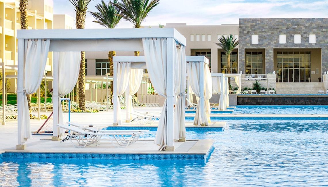 Außenbereich des Jaz Aquaviva Hotels mit Swimmingpools und Liegestühlen unter weißen Vorhängen.