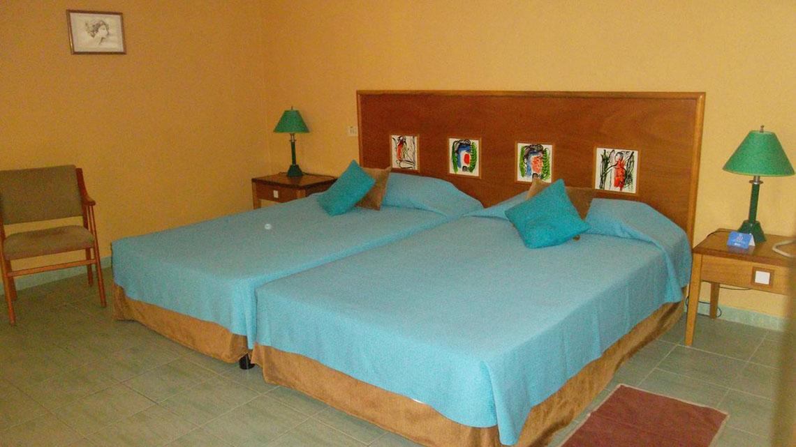 Zwei Betten mit blauen Laken in einem gelben Schlafzimmer des ROC Arenas Doradas Hotels.
