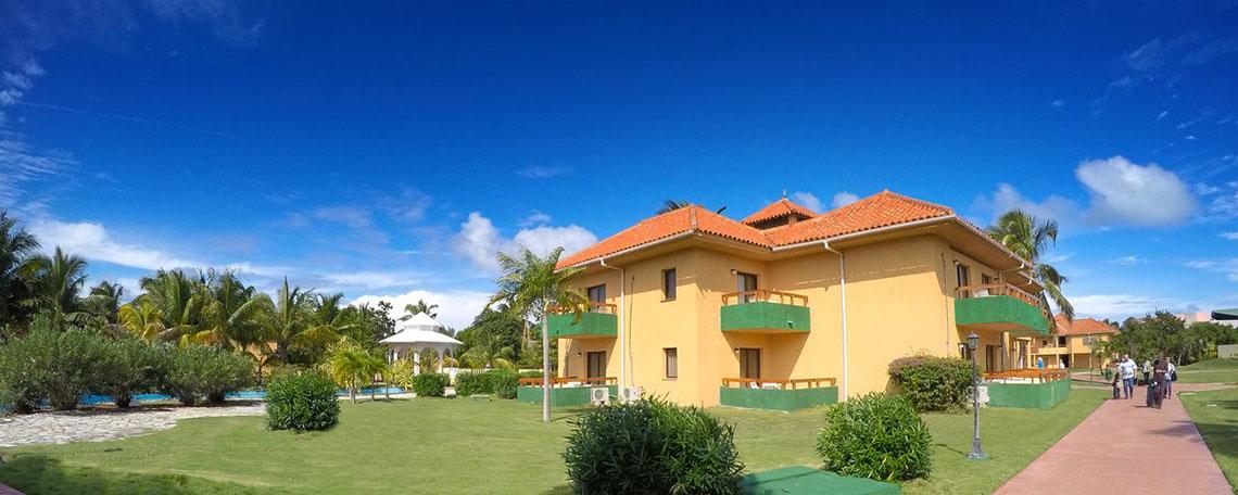 Außenansicht des ROC Arenas Doradas Hotels mit gelben Wänden und grünen Balkonen vor einem blauen Himmel.
