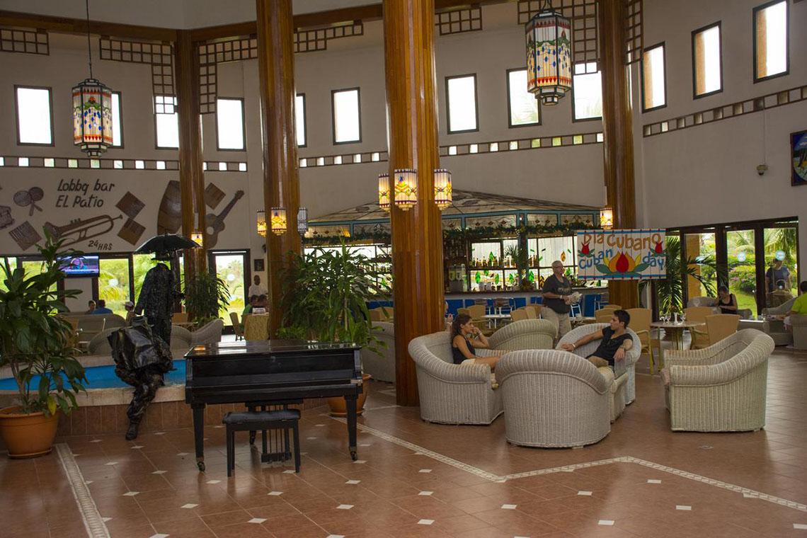Hotellobby mit schwarzem Klavier und wei ßen Sofas, beleuchtet von hängenden Lampen.