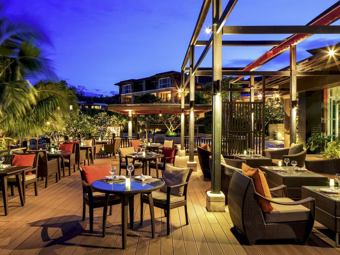 Terrasse des Pullman Phuket Panwa Beach Resort mit abendlicher Atmosphäre, Tischen und Stühlen im Freien.