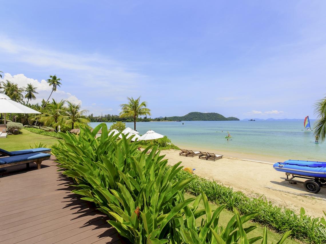 Aussicht auf den Strand des Pullman Phuket Panwa Beach Resort mit Sonnenliegen und Palmen.