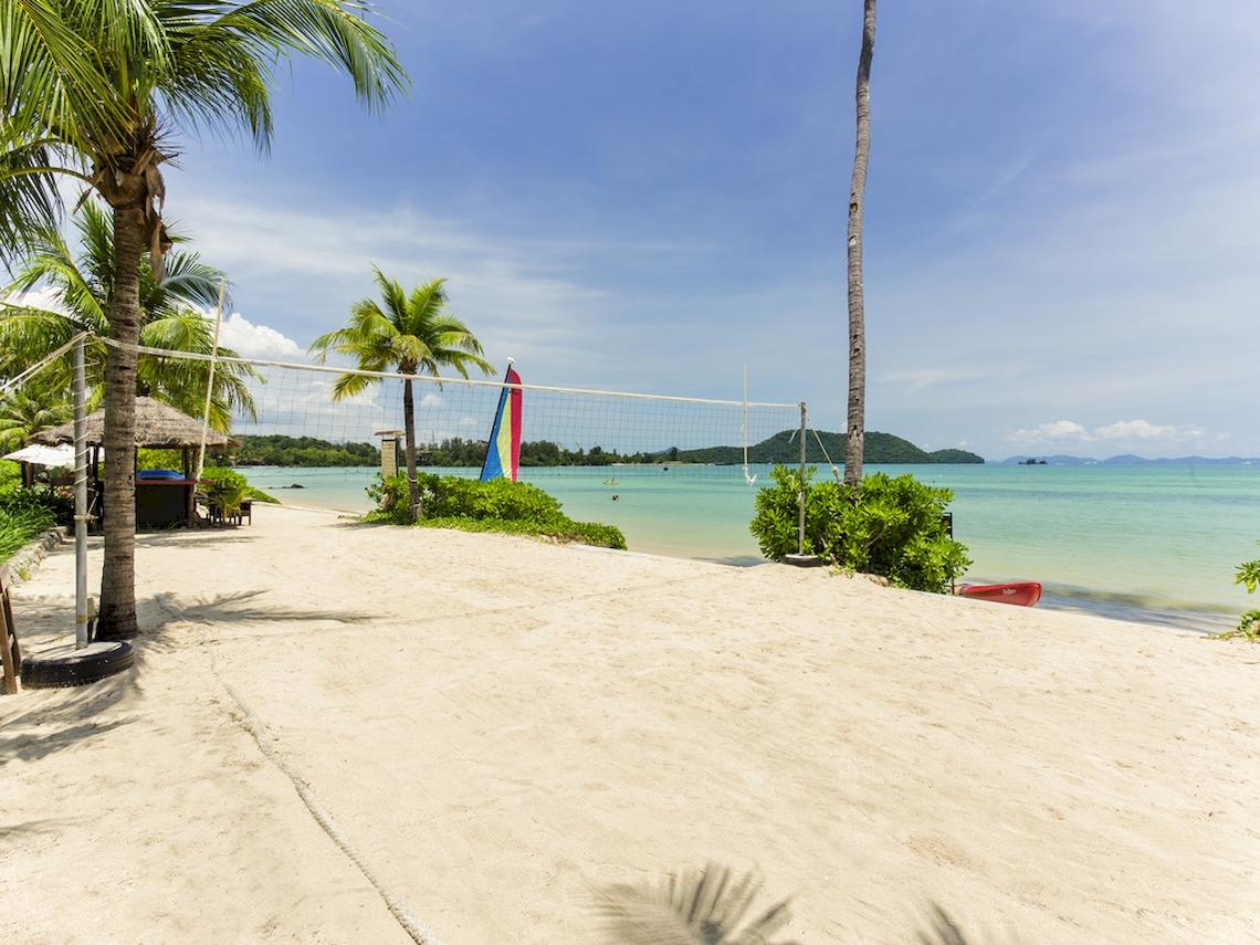 Ein Volleyballplatz am Strand des Pullman Phuket Panwa Beach Resort mit Palmen und Meer im Hintergrund.
