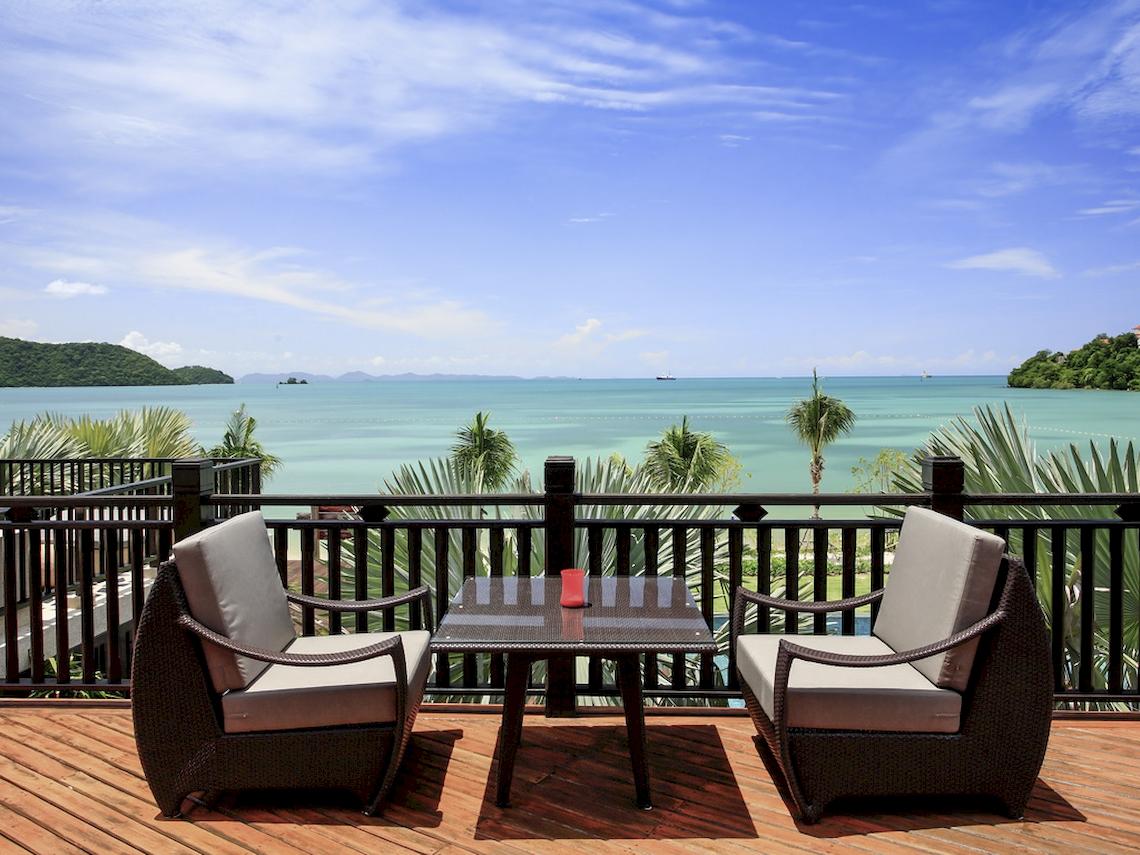 Ausblick auf das Meer von der Terrasse des Pullman Phuket Panwa Beach Resort mit zwei Rattan-Stuhls und einem Tisch.