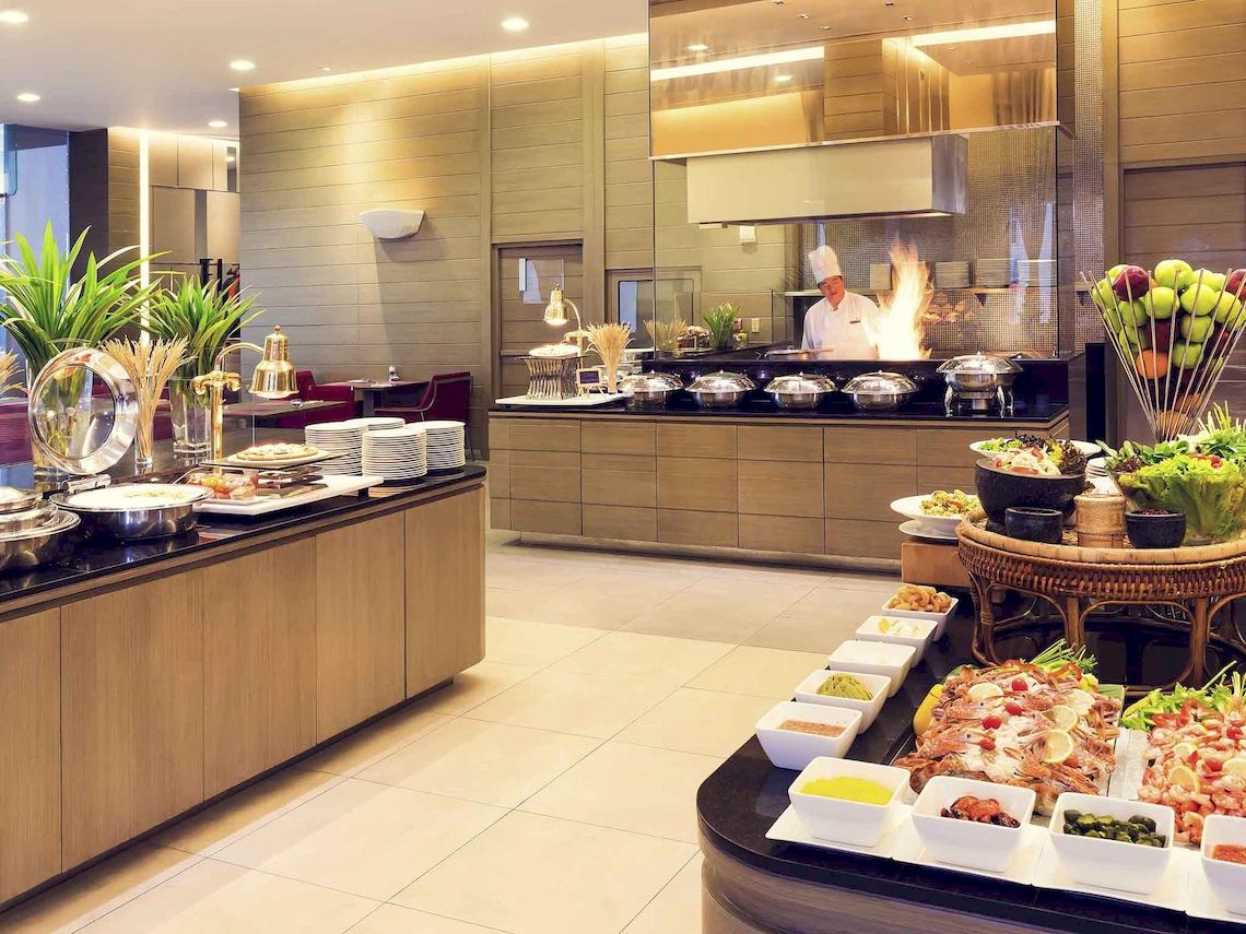 Buffet im Restaurant des Mercure Bangkok Siam Hotels mit verschiedenen Gerichten und einem Koch am Grill.