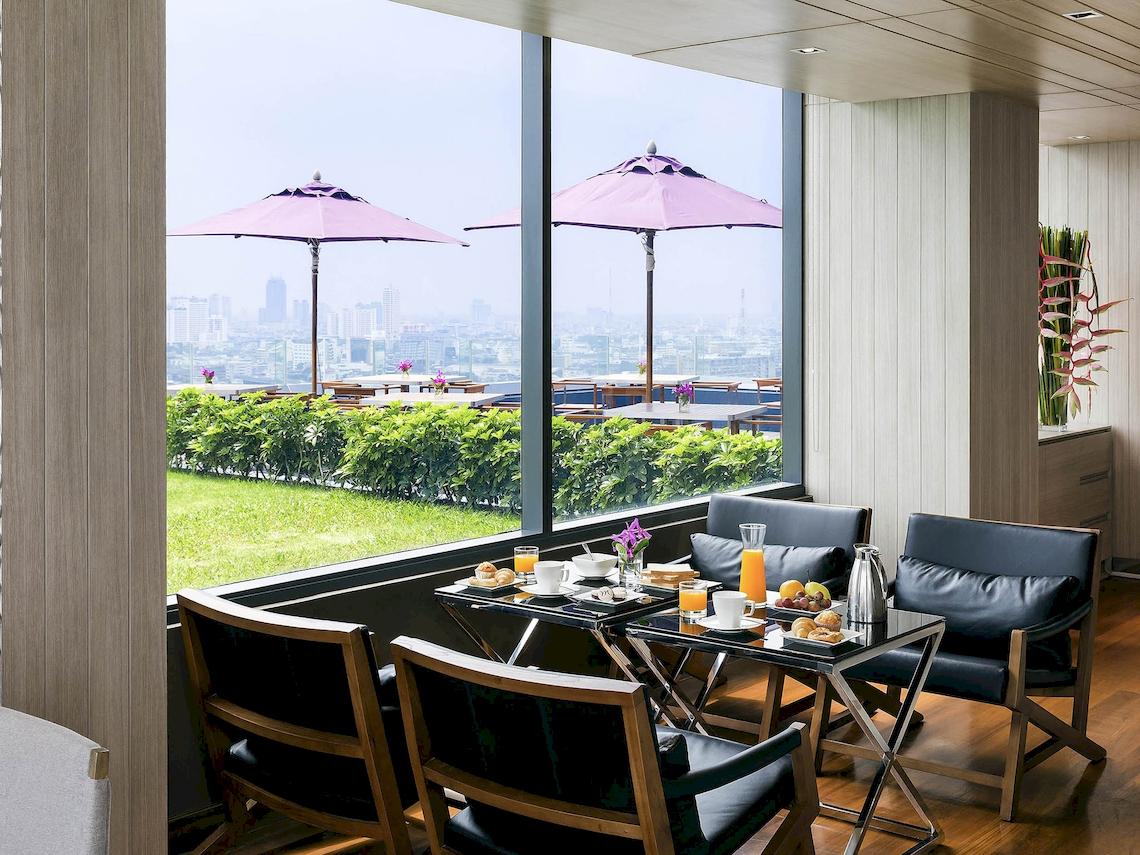 Frühstückstisch im Mercure Bangkok Siam mit Blick auf die Stadt und grüner Rasenfläche draußen.