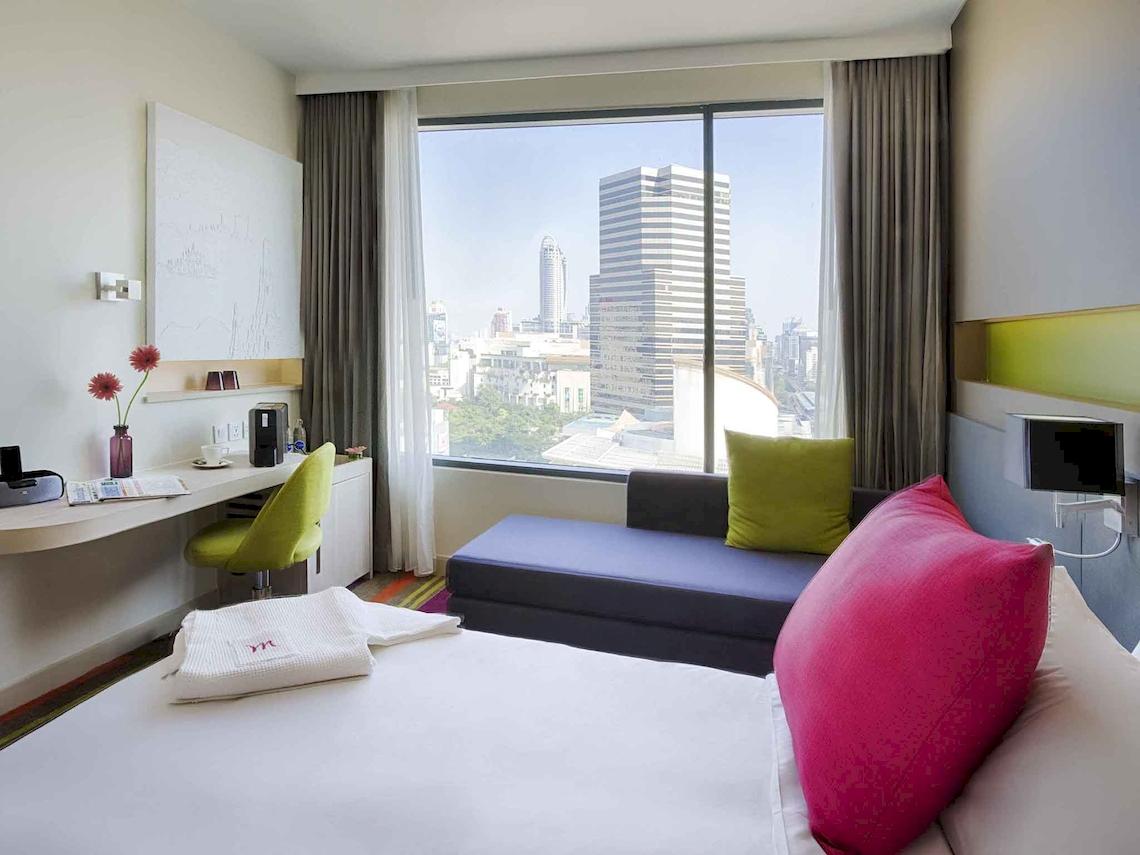 Ein Zimmer im Mercure Bangkok Siam Hotel mit Blick auf die Stadt, einem Bett, einem Schreibtisch und einem Fenster mit Ausblick.