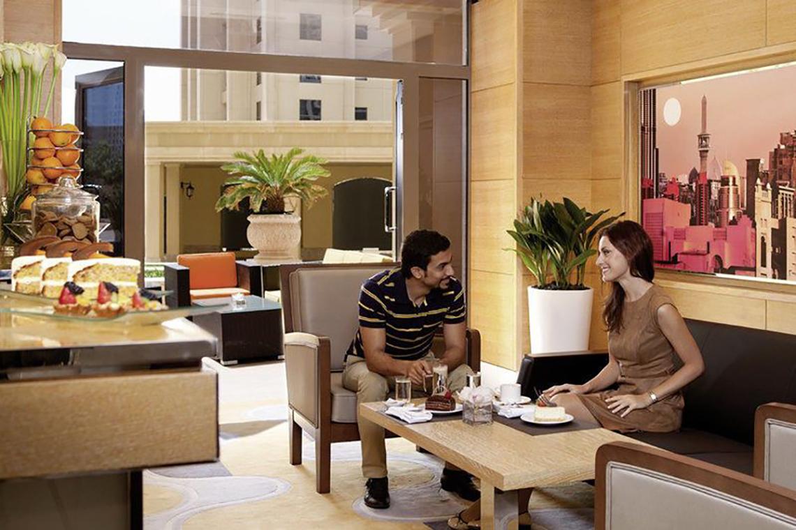 Loungebereich im Delta Hotels by Marriott Jumeirah Beach, Dubai, mit einem Paar, das auf einem Sofa sitzt und auf eine Stadtansicht schaut.
