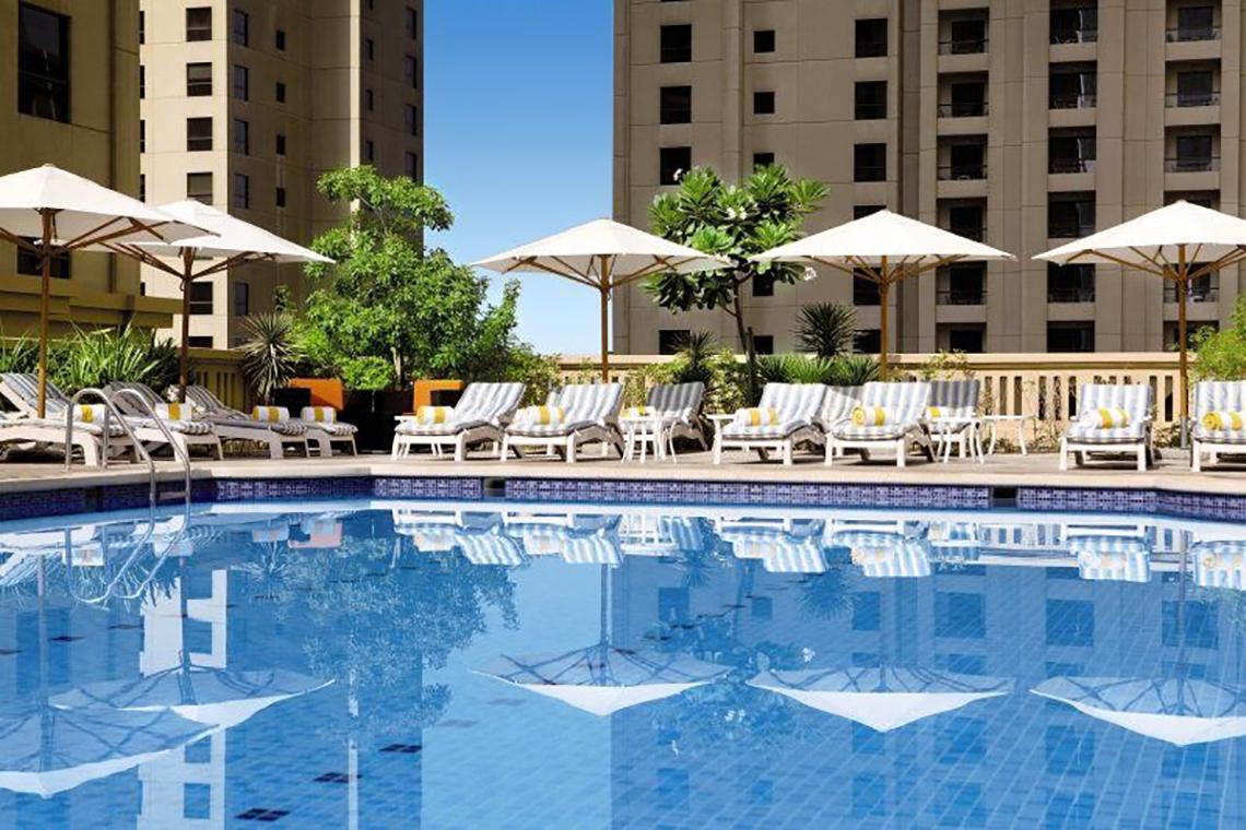 Außenpool des Delta Hotels by Marriott Jumeirah Beach in Dubai mit Sonnenliegen und Sonnenschirmen.