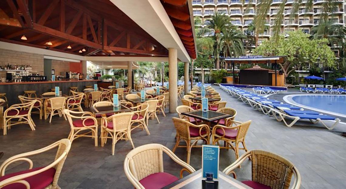 Hotellounge des Barcelo Margaritas mit Tischen, Stühlen und Pool im Hintergrund.