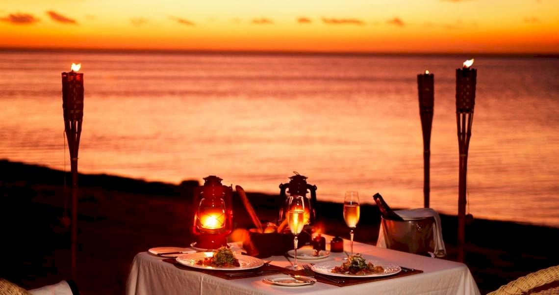 Dinnertisch am Strand bei Sonnenuntergang mit Gläsern und Speisen