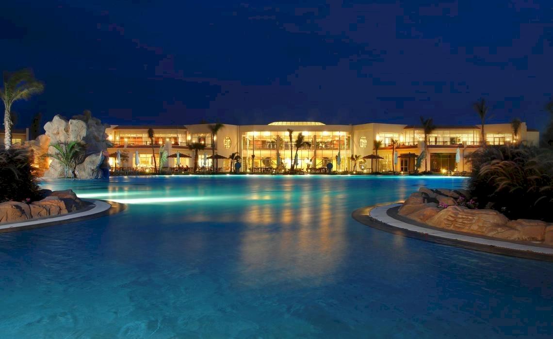 Poolansicht des DoubleTree by Hilton Sharks Bay Resort bei Nacht mit beleuchtetem Gebäude.