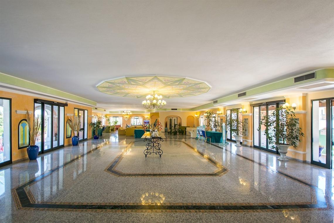Empfangsbereich des Club Hotel Marina Beach mit hellem Innendesign, großen Fenstern und Dekorationspflanzen.