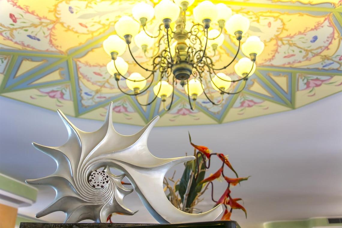 Ein Hotel-Lobby mit einer großen, silbernen Muschelskulptur und einer kunstvollen Deckenlampe.