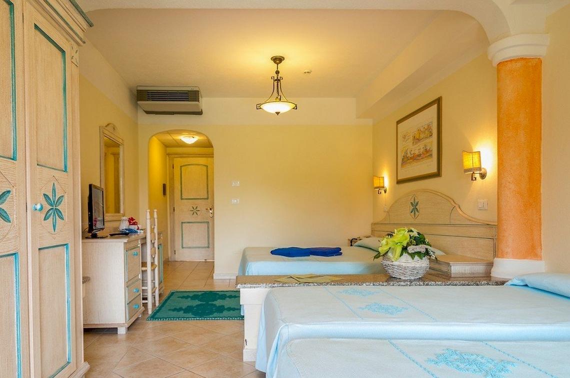 Innenansicht eines Doppelzimmers im Club Hotel Marina Beach mit zwei Betten, Nachttischen und Dekor.