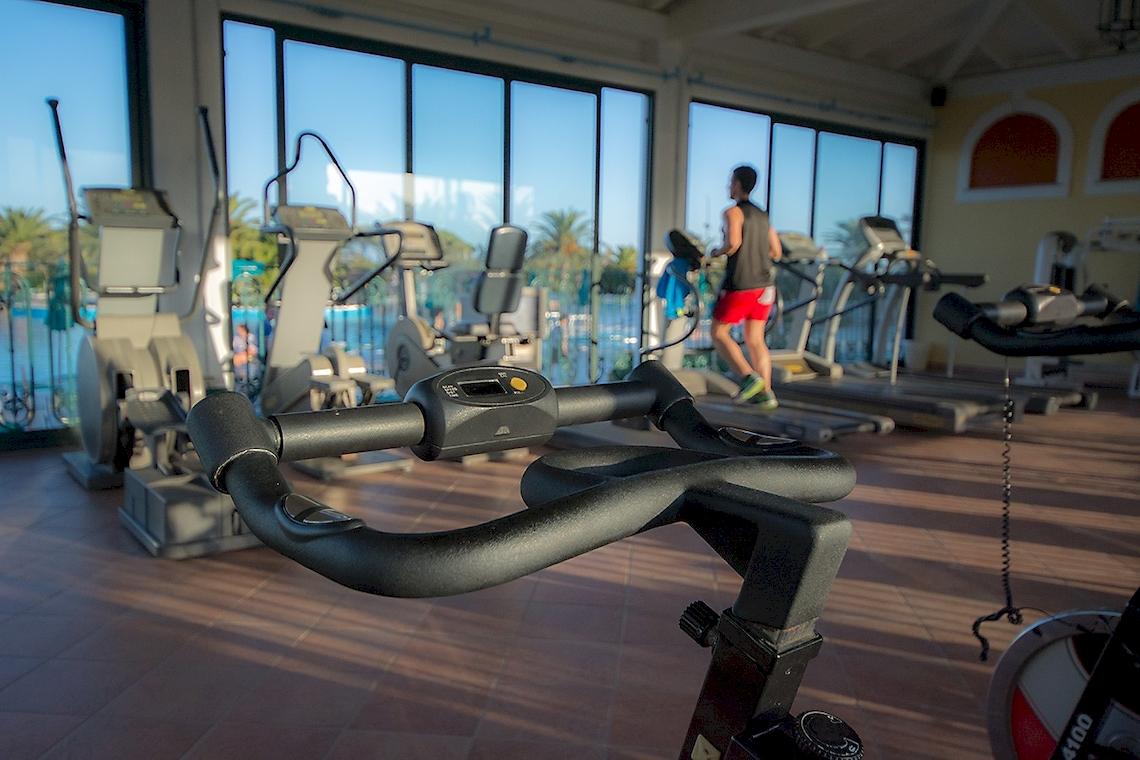 Fitnessstudio im Club Hotel Marina Beach mit Geräten und einem Mann, der auf einem Laufband läuft.