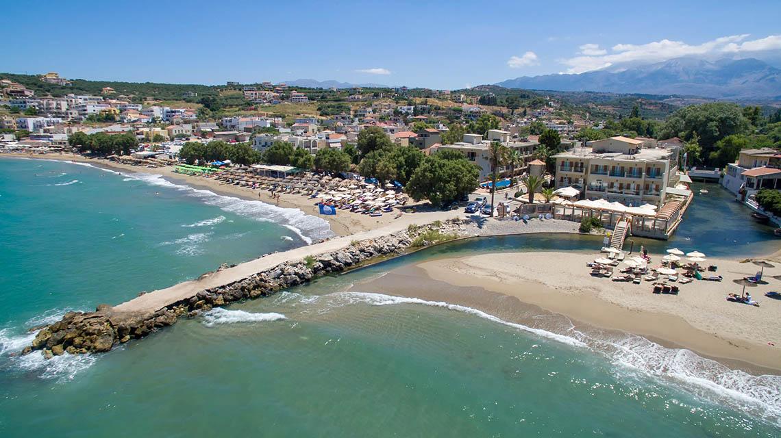 Luftaufnahme des Kalyves Beach Hotels mit Strand, Gebäuden und umliegender Landschaft.