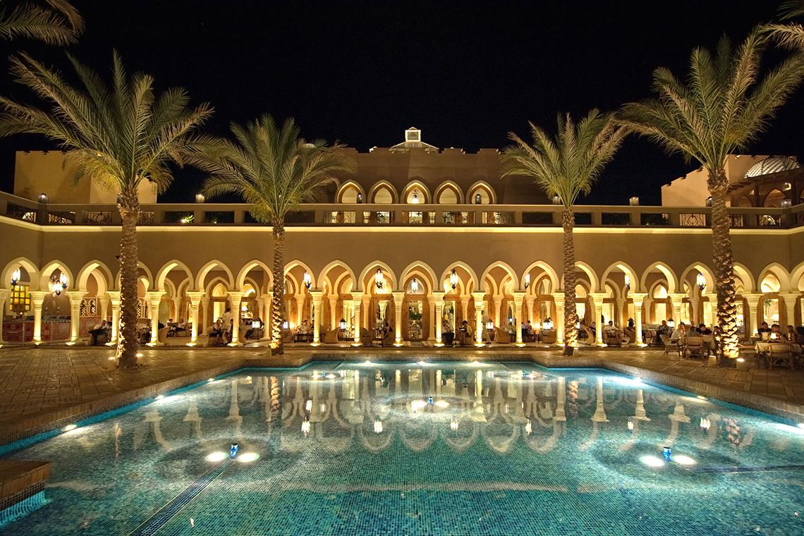 Nachtansicht des Grand Makadi Hotels mit Pool und Palmen, beleuchtete Arkaden im Hintergrund.