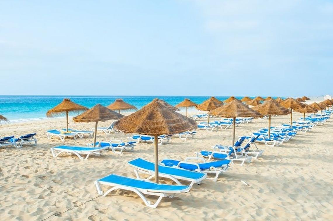 Strandszene im Oasis Belorizonte Hotel mit vielen Sonnenliegen und Sonnenschirmen.