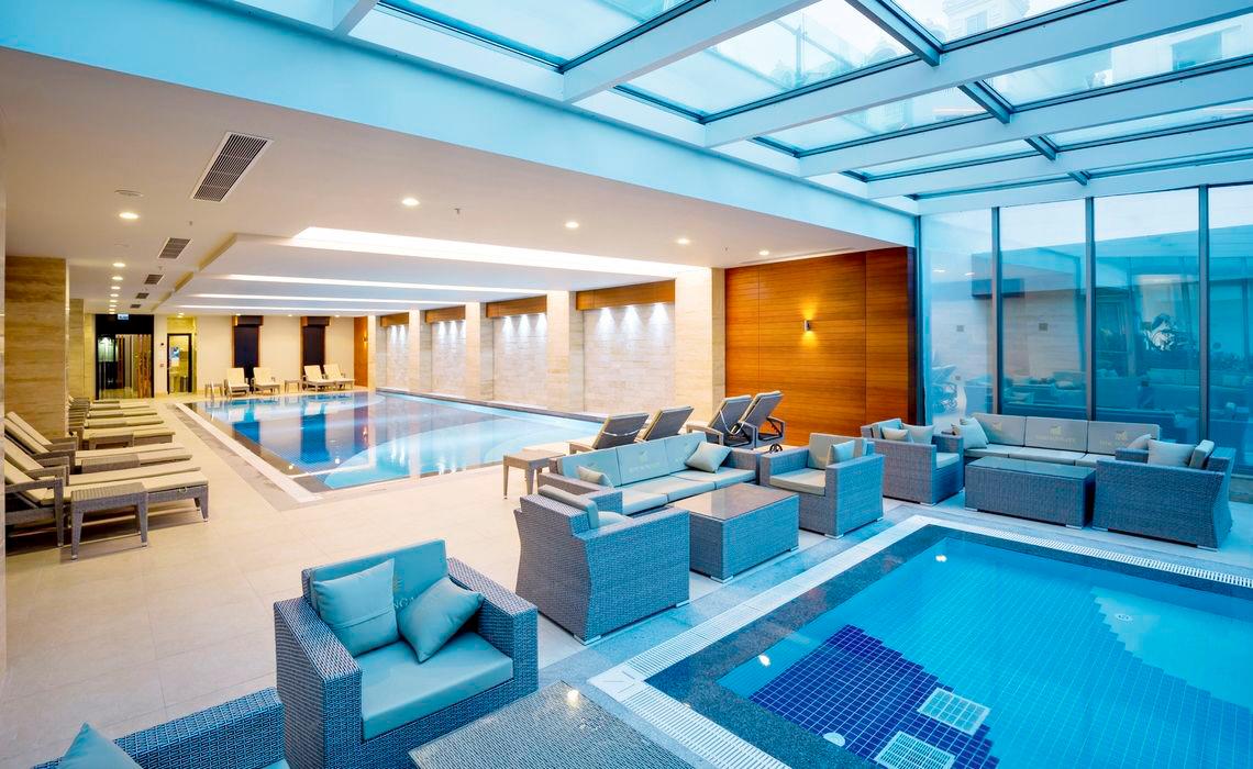 Innenpool des Side Sunport Hotel & Spa mit Loungebereich und Sonnenliegen.