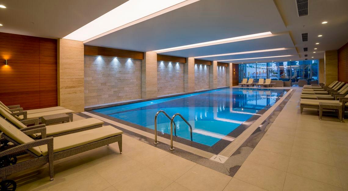 Innenpool des Side Sunport Hotel & Spa mit Lounge-Sesseln und blauem Wasser.