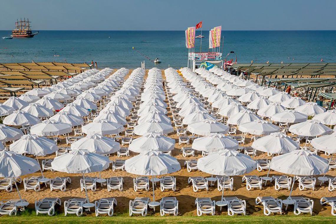 Strand mit vielen weißen Sonnenschirmen und Liegen am Meer