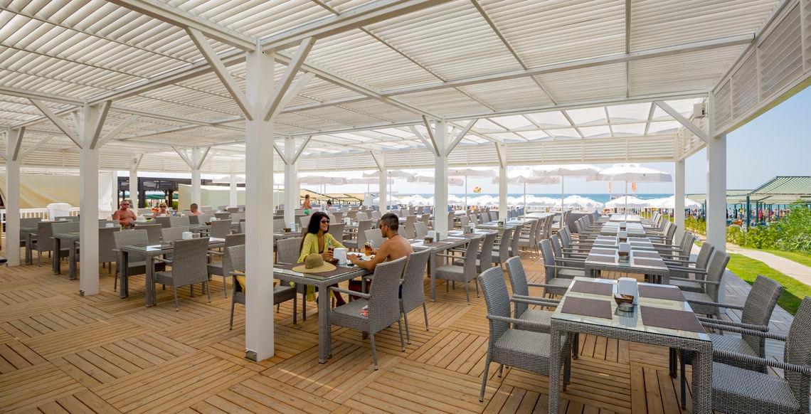Terrasse des Side Sunport Hotel & Spa mit Gästen, Tischen und Stühlen, Blick aufs Meer.