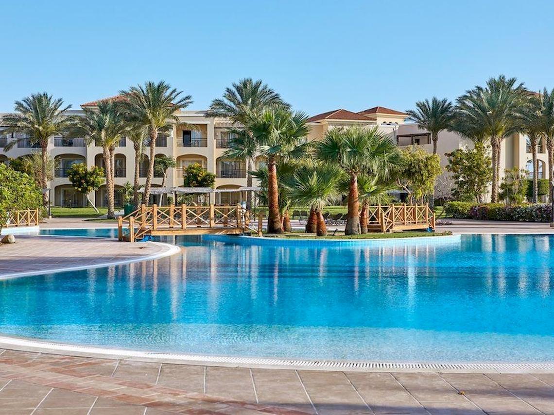 Außenpool des Jaz Mirabel Beach Hotels mit Gebäuden und Palmen im Hintergrund.
