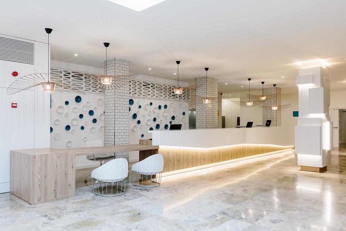 Empfangsbereich des Leonardo Royal Hotel Ibiza Santa Eulalia mit modernem Design, Marmorboden und weißen Möbeln.