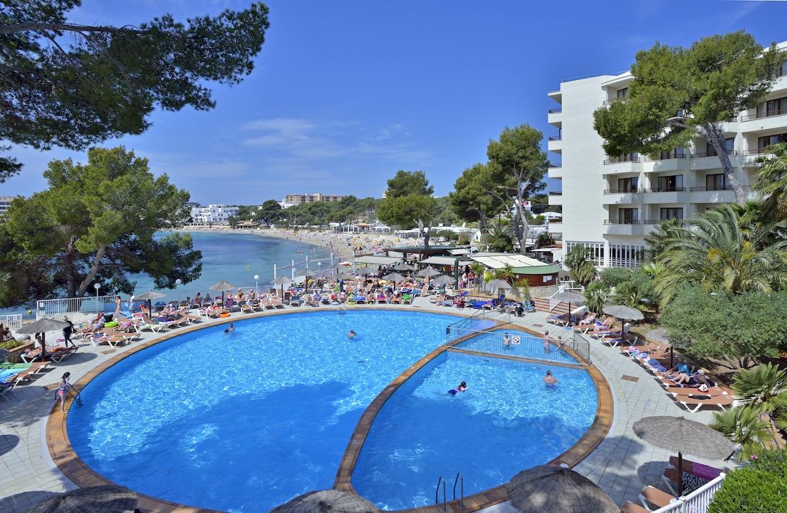 Außenpoolbereich des Leonardo Royal Hotel Ibiza Santa Eulalia mit vielen Gästen und einer schönen Aussicht auf den Strand.