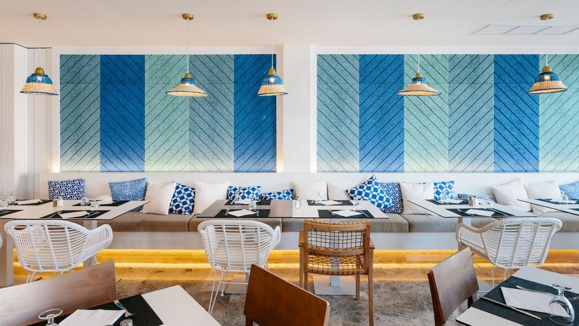 Speisebereich im Leonardo Royal Hotel Ibiza Santa Eulalia mit blauen und weißen Wandmustern und weißen Stühlen.