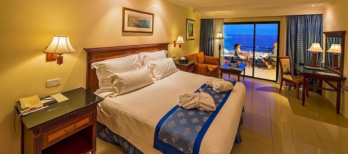 Ein Hotelzimmer im Grand Hotel Gozo mit einem großen Bett, Fenstern und einem Blick auf das Meer.