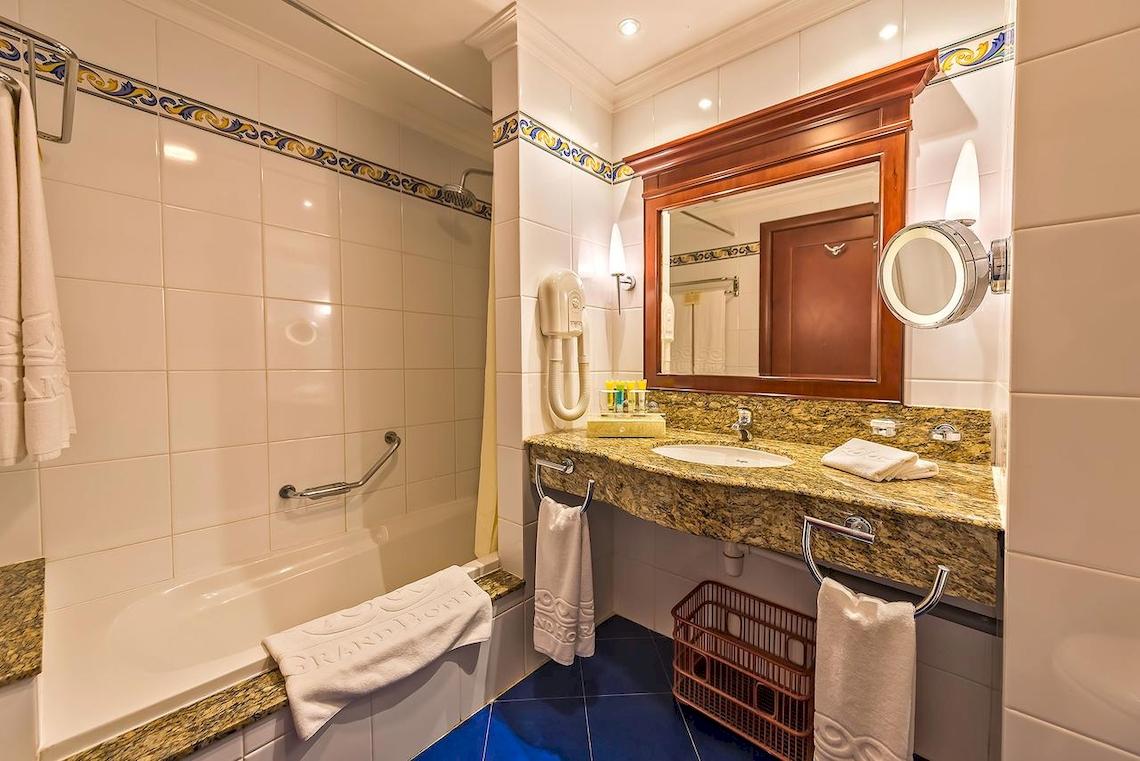 Badezimmer im Grand Hotel Gozo mit Badewanne, Waschbecken und Spiegel.