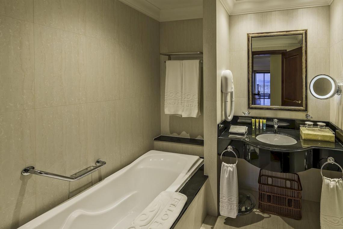Badezimmer im Grand Hotel Gozo mit Badewanne, Waschbecken und Spiegeln.