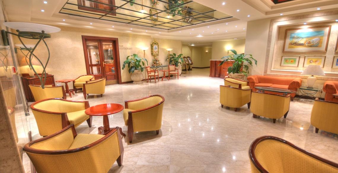 Lobby des Grand Hotel Gozo mit gelben Stühlen, Tischen, Pflanzen und Couchgarnitur.