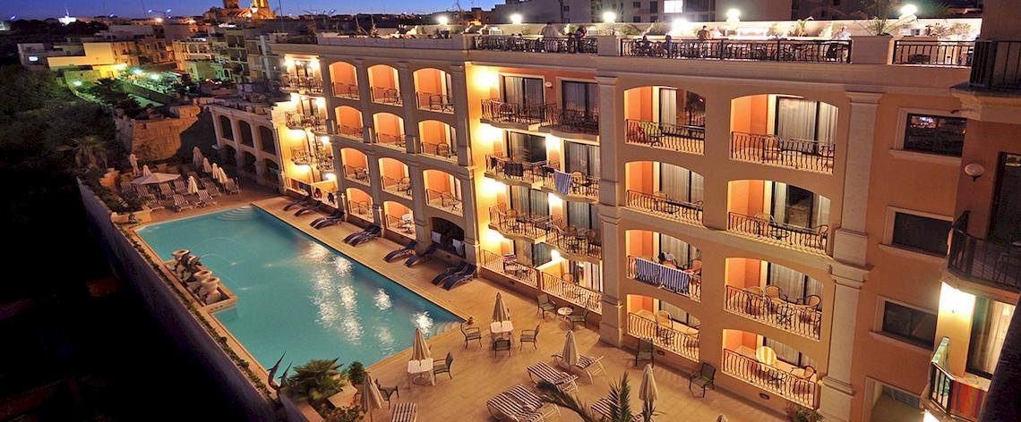 Abendliche Außenansicht des Grand Hotel Gozo mit Swimmingpool und beleuchteten Terrassen.